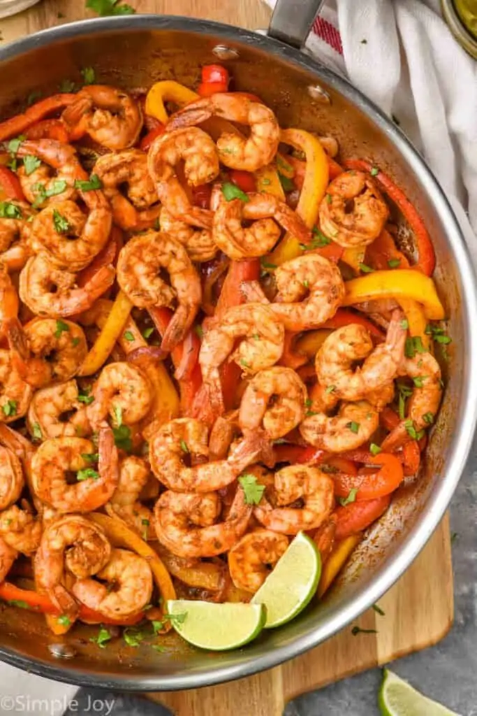 overhead view of a skillet full of shrimp fajita fillings garnished with fresh cilantro and two lime wedges