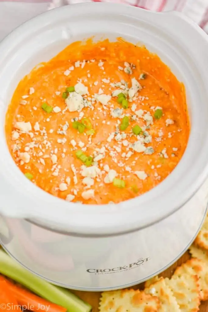 overhead view of a small crockpot with buffalo chicken dip and garnished with blue cheese and diced scallions
