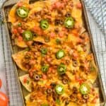 overhead view of a sheet pan nachos garnished with tomatoes, cilantro, olives, and jalapeños - 7