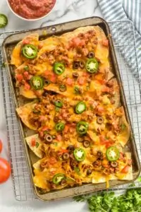 overhead view of a sheet pan nachos garnished with tomatoes, cilantro, olives, and jalapeños