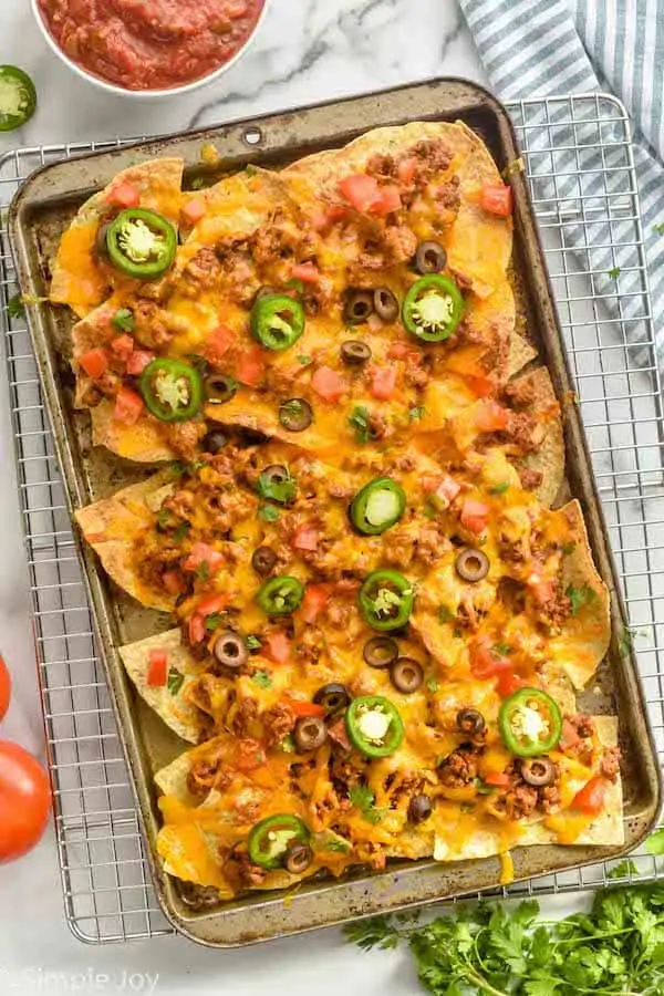 overhead view of a sheet pan nachos garnished with tomatoes, cilantro, olives, and jalapeños