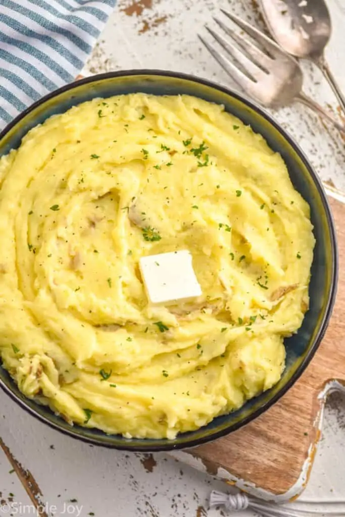 overhead photo of mashed potatoes in a dark bowl with a pad of butter and garnished with parsley and pepper