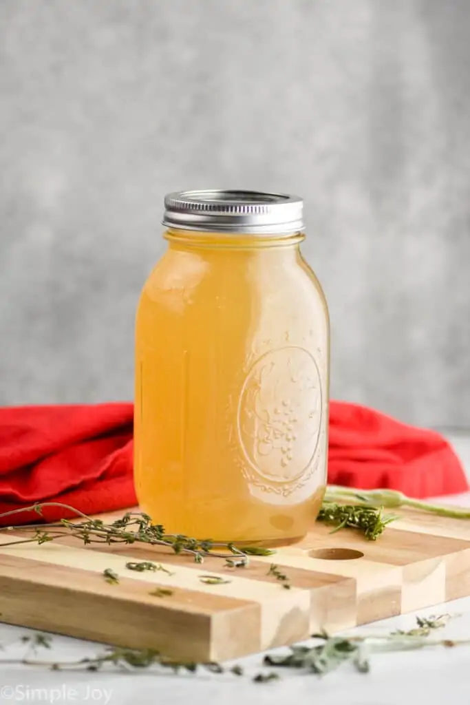 a mason jar full of turkey broth on a cutting board surrounded by fresh herbs