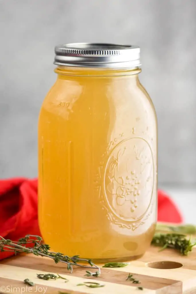 a mason jar full of turkey broth on a cutting board surrounded by fresh herbs