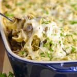 a spoon pulling out a cheesey spoonful of turkey tetrazzini from the casserole dish
