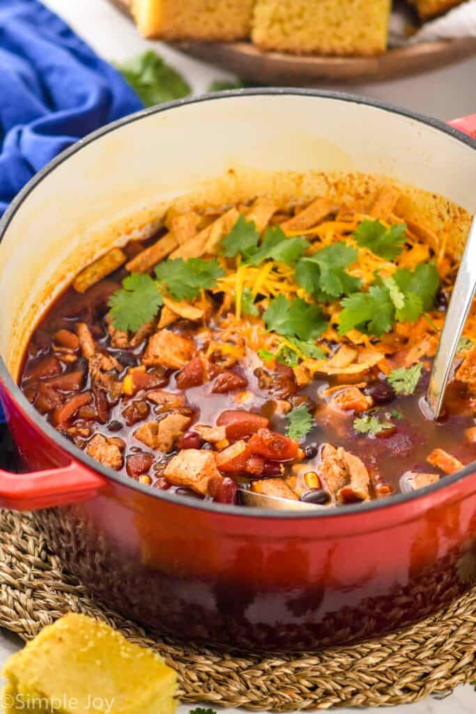 a red stock pot full of turkey tortilla soup recipe with tortilla strips and cilantro on top with cornbread around it
