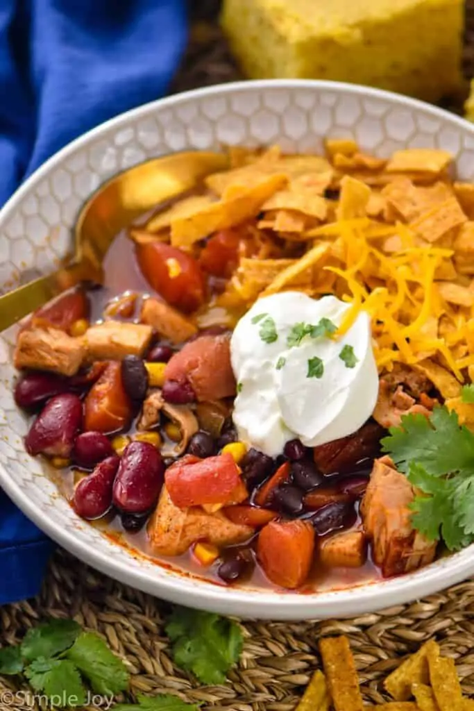 close up view of a bowl of turkey tortilla soup garnished with tortilla strips, shredded cheese, sour cream, and cilantro