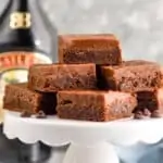 a white cake stand with a pile of baileys brownies, a bottle of baileys in the background