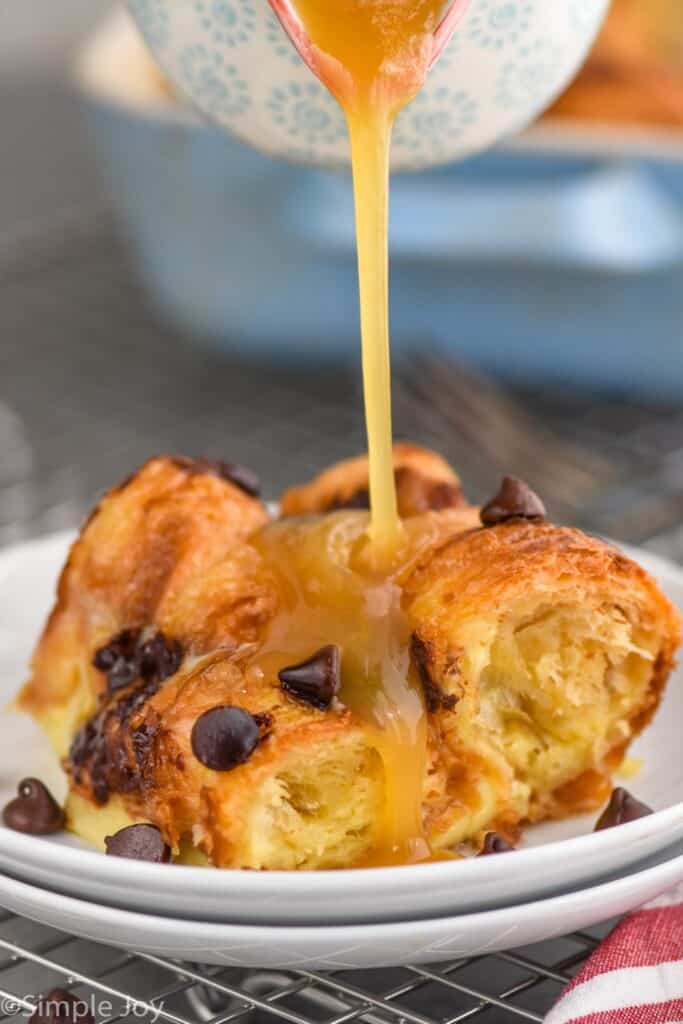 brown sugar sauce being poured over a piece of croissant bread pudding recipe on a small white plate