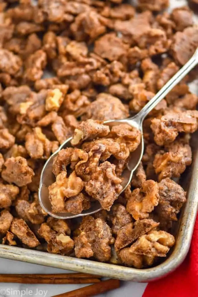 a spoon dishing up candied walnuts recipe from a baking sheet