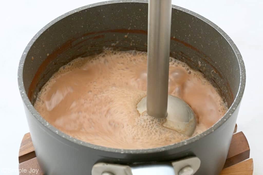 Immersion blender mixing salted caramel mocha ingredients in a saucepan