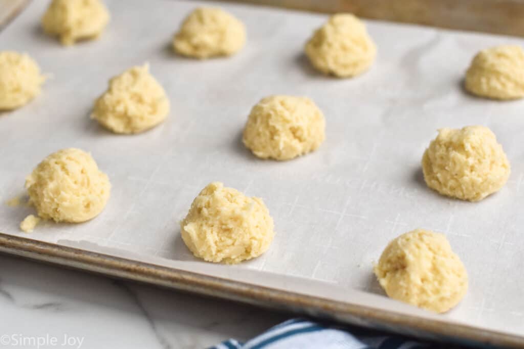 sour cream cookie dough balls on a parchment lined baking sheet before baking