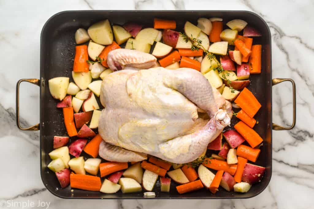 a raw chicken on top of some seasoned vegetables in a roasting pan