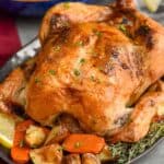 close up of a roast chicken on a platter surrounded by vegetables