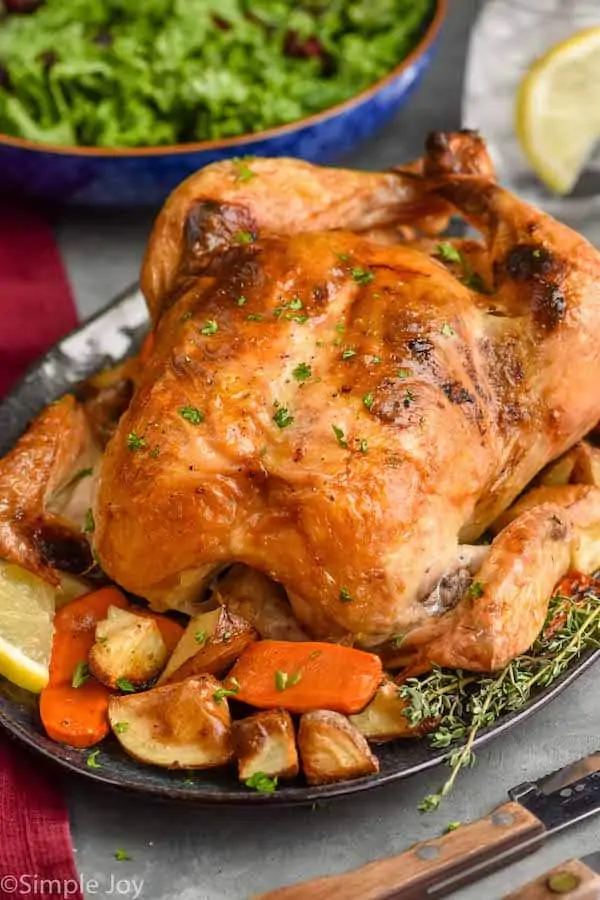 close up of a roast chicken on a platter surrounded by vegetables