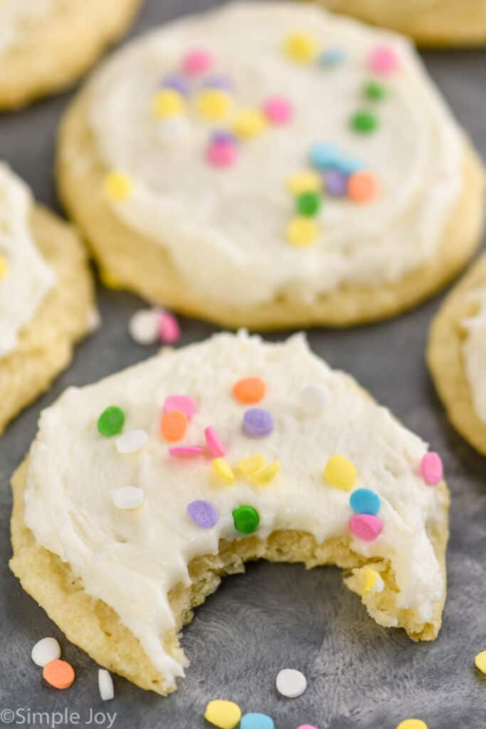 close up of a sour cream cookie recipe that has been frosted and decorated with rainbow sprinkles with a bite missing