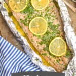overhead view of baked salmon recipe that is in foil and topped with lemon slices fresh parsley and has two forks next to it