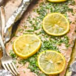 side view of baked salmon in foil that has been topped with lemon slices and fresh parsley