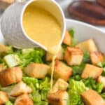 Caesar salad dressing being poured over a caesar salad with the name of the recipe on the photo