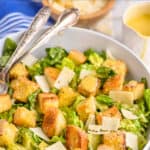 side view of a Caesar salad in a bowl with large croutons and peels of Parmesan cheese with the name of the recipe above the photo