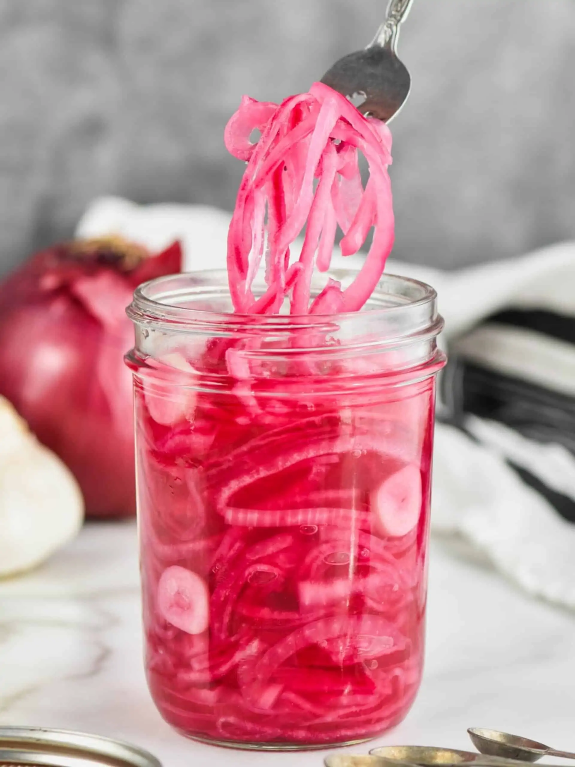 a fork pulling pickled red onions out of a jar