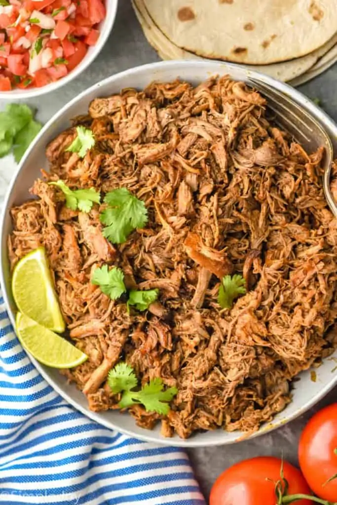 overhead view of slow cooker carnitas meat that has been garnished with two limes and fresh cilantro
