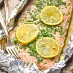 side view of baked salmon in foil that has been topped with lemon slices and fresh parsley