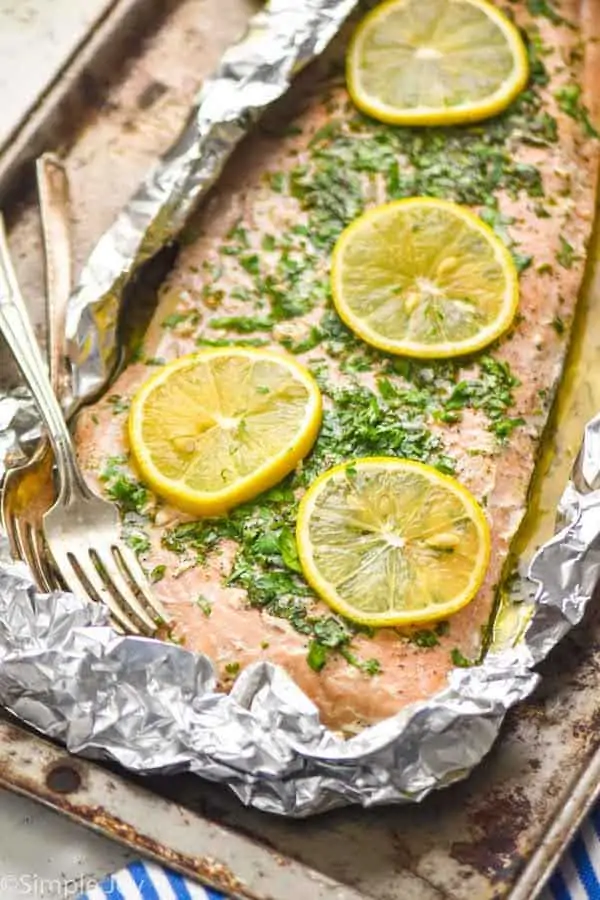 side view of baked salmon in foil that has been topped with lemon slices and fresh parsley