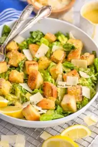 side view of a Caesar salad in a bowl with large croutons and peels of Parmesan cheese