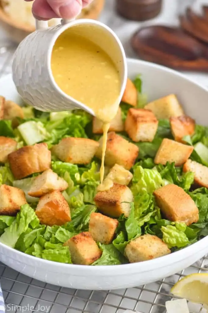 Caesar salad dressing being poured over a caesar salad