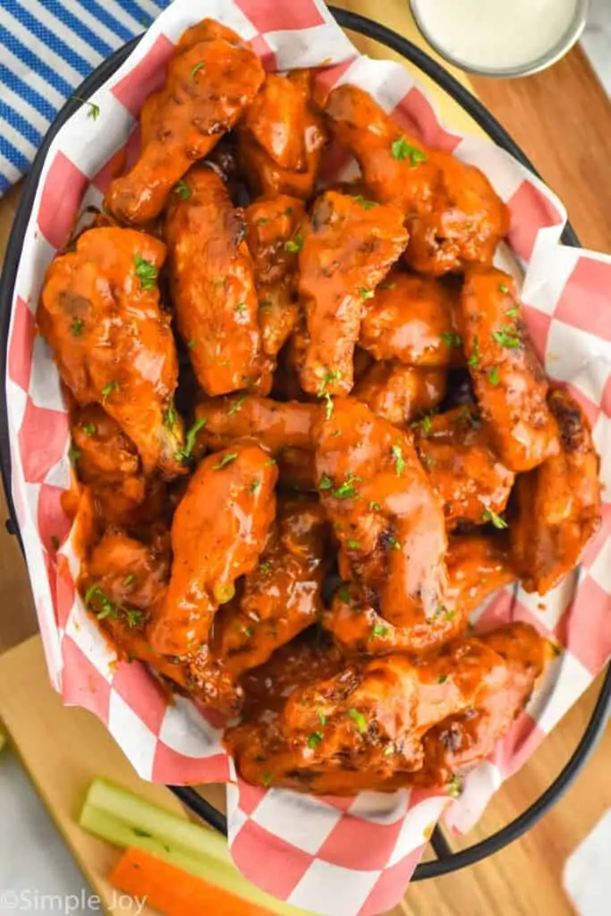 overhead view of air fryer chicken wings that have been tossed in sauce and are in a basket for serving