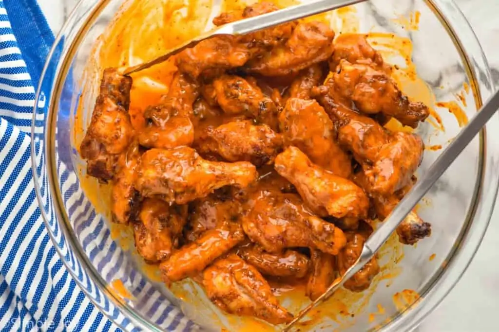 bowl of chicken wings being tossed with buffalo sauce