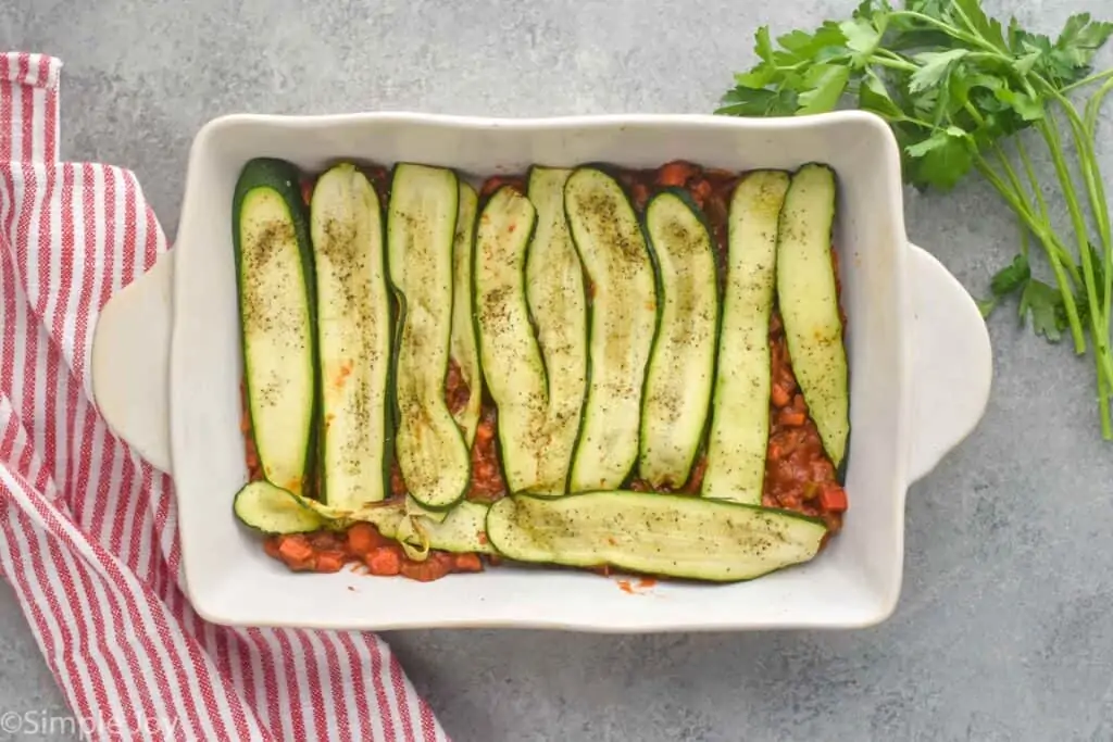 overhead picture of a baking dish with a layer of sauce topped with the first layer of zucchini to make zucchini lasagna