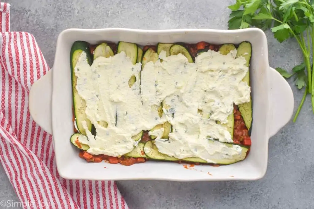 overhead view of zucchini lasagna being constructed, can see ricotta mixture on top of roasted zucchini