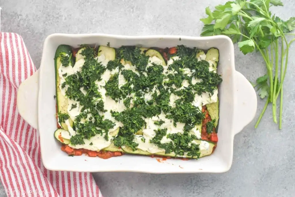 overhead view of zucchini lasagna being put together, can see chopped spinach on top of ricotta layer