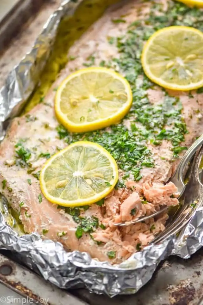 oven baked salmon in foil topped with lemon slices and parsley that has been lightly flaked by two forks