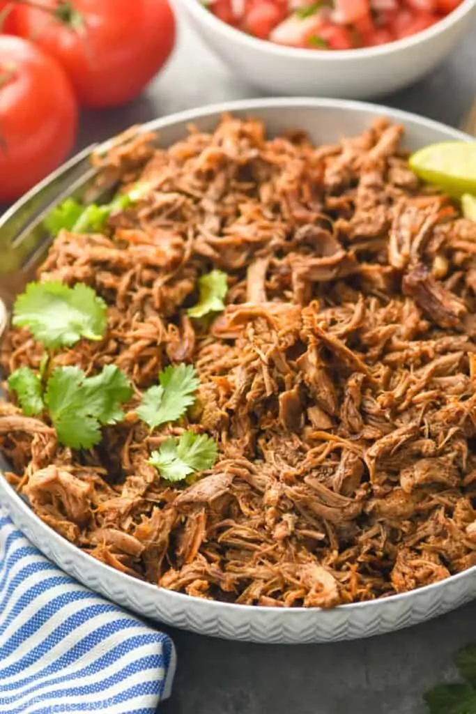 bowl of slow cooker pork carnitas meat that has been garnished with cilantro and limes