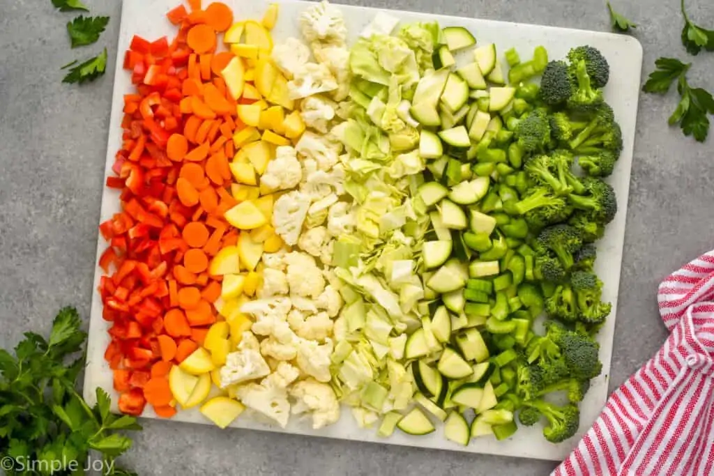 overhead view of vegetables chopped up to make vegetable soup on a cutting board in rainbow order