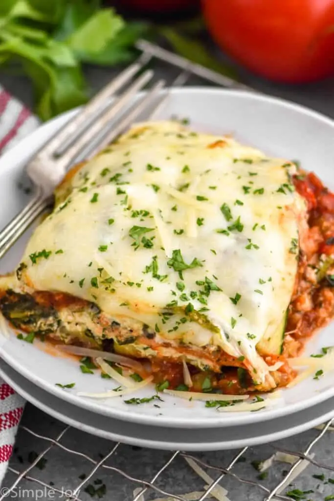 a close up of a piece of zucchini lasagna on white plates topped with freshly chopped parsley