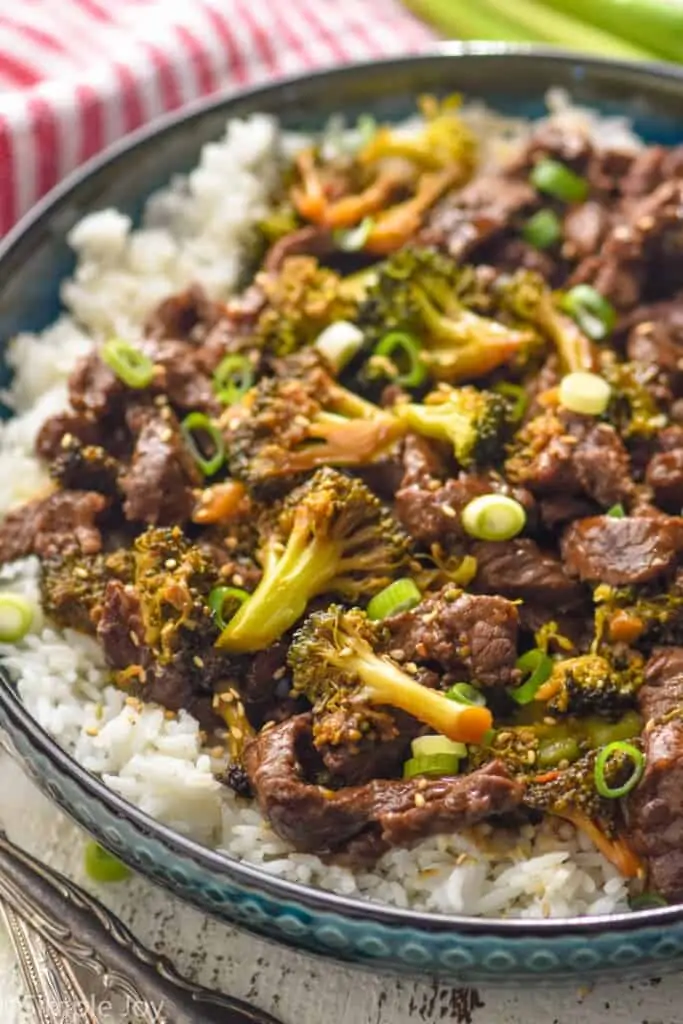 side view of a bowl of beef and broccoli over rice garnished with sesame seeds and sliced scallions