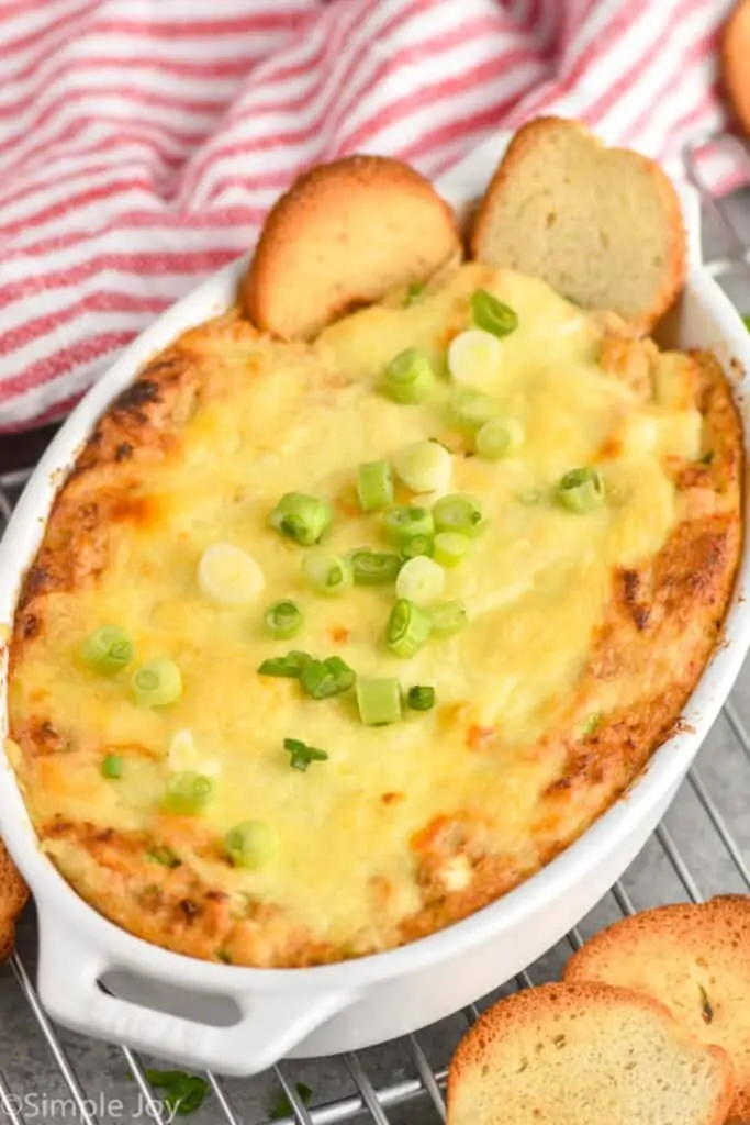 white casserole dish full of hot crab dip with two bagel chips sticking out of it