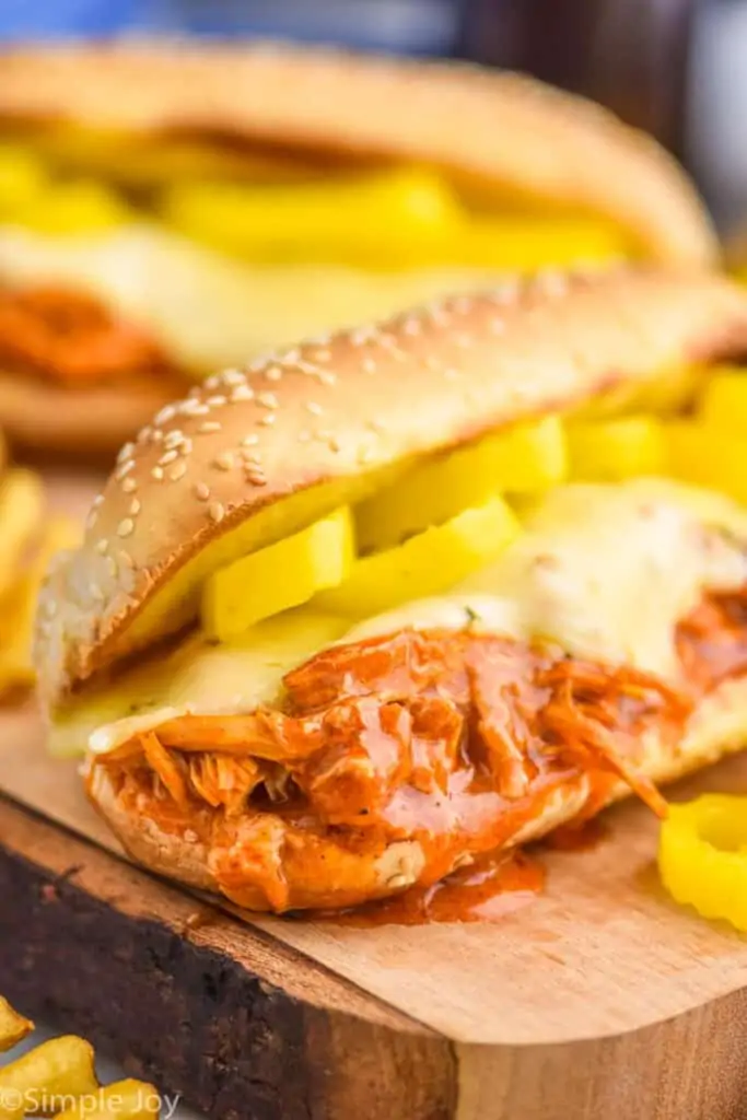 close up of a crockpot buffalo chicken sandwich on a hoagie roll with melted cheese and pepper rings