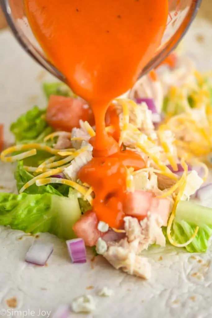 buffalo sauce being poured over ingredients for a buffalo chicken wrap