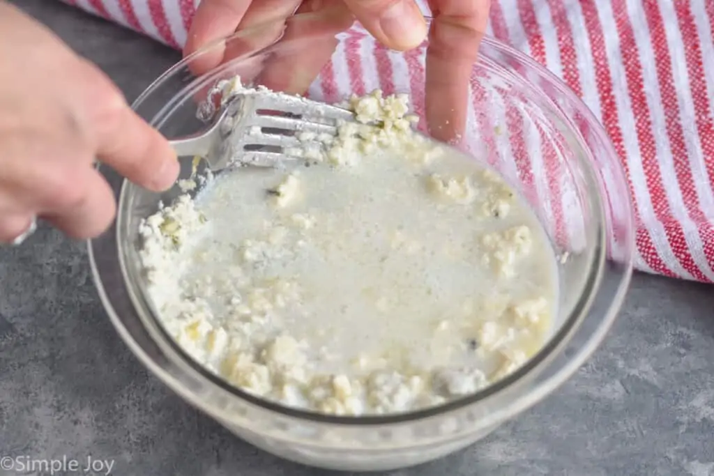 blue cheese and milk mixture being mashed together with a fork for how to make blue cheese dressing