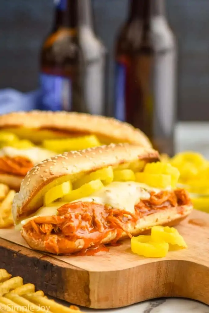 crockpot buffalo chicken sandwich with cheese and pepper rings on a cutting board