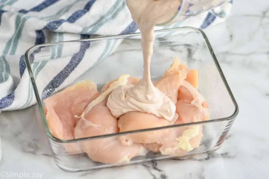 sour cream marinade being poured over a small container full of chicken cutlets