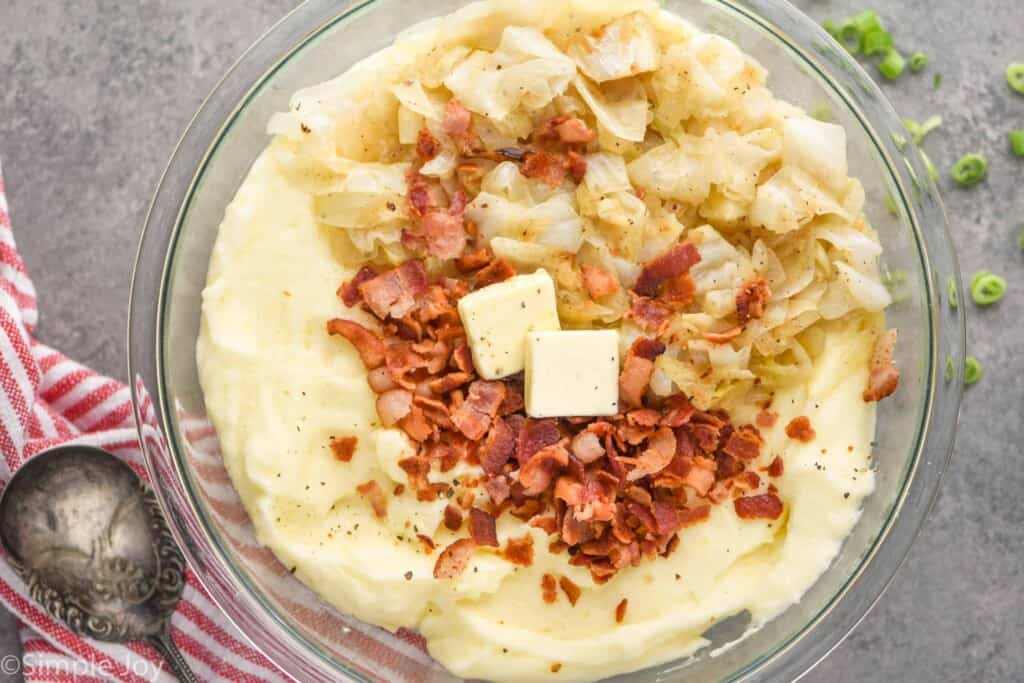 overhead of a bowl of mashed potatoes with cooked bacon crumbles and sautéed cabbage on top