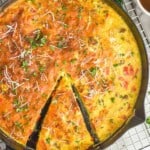 overhead of a frittata with a piece partially cut out, garnished with parsley and parmesan