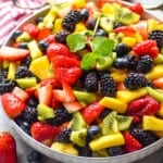 fruit salad in a bowl that is topped with a mint leaf sprig
