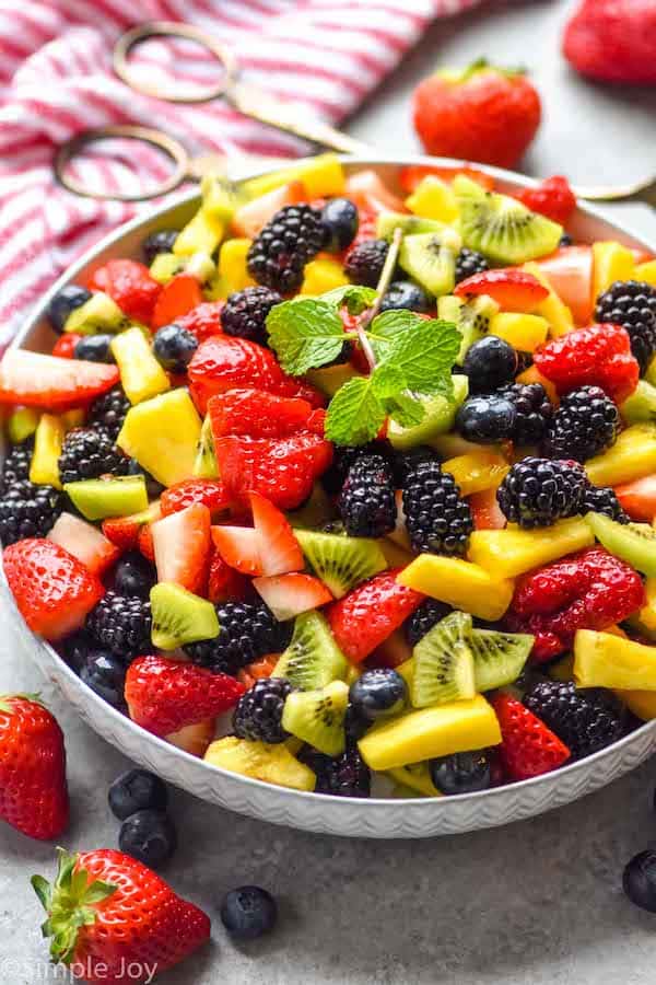 fruit salad in a bowl that is topped with a mint leaf sprig